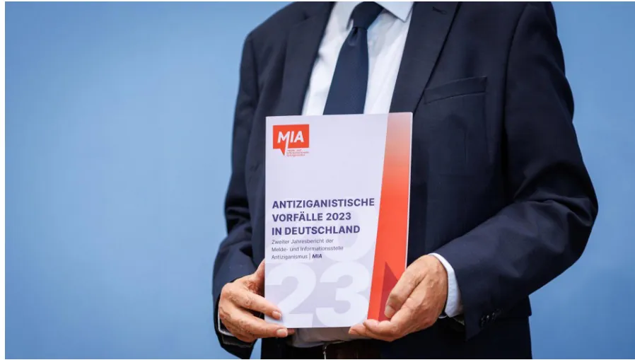 Die Broschüre des MIA Jahresberichts 2023 wird vor dem Oberkörper gehalten.